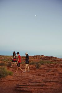 Full length of friends standing on landscape against clear sky