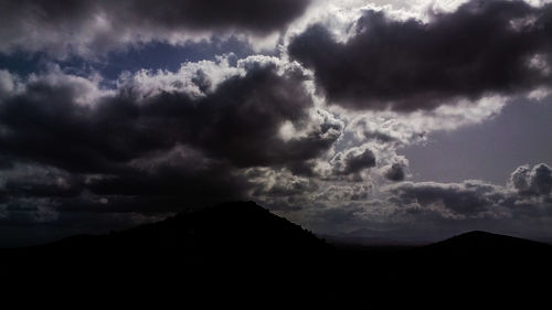 Low angle view of storm clouds over silhouette landscape