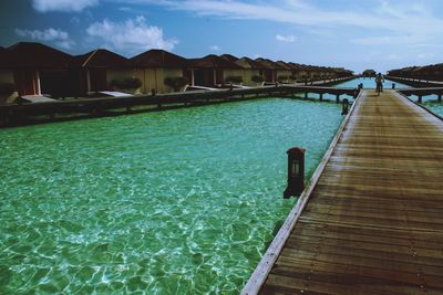 Pier over swimming pool by building against sky