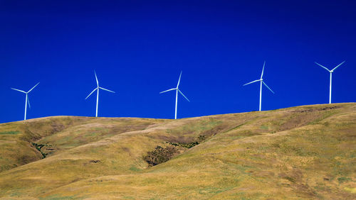 Wind turbines on field against blue sky