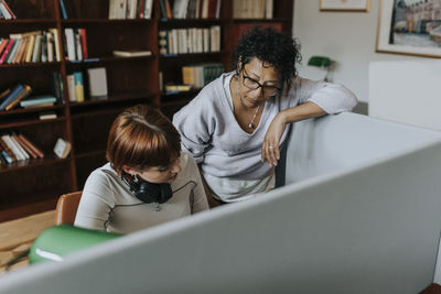 Teacher standing by female teenage student in library