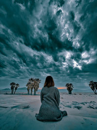 Rear view of woman sitting on snow covered land