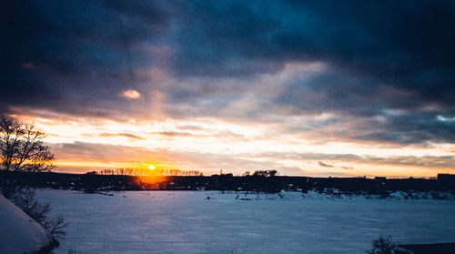 Silhouette trees by frozen lake against sky during sunset