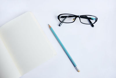 High angle view of eyeglasses and pencil on white background