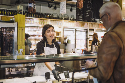 Saleswoman gesturing while talking with senior male customer at convenience store