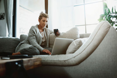 Low angle view of woman using laptop while sitting on sofa at home