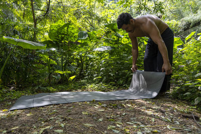 Young latin man arranging his yoga mat, inside a forest on a plain, direct contact with nature