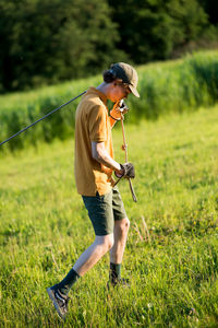 Side view of young man holding rope while standing on grassy field at park during sunset