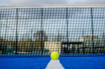 Ground level view of a ball on the line of a blue paddle tennis court with the net out of focus 