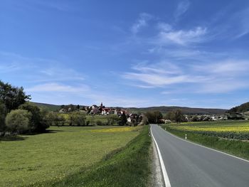 Empty road amidst field against sky