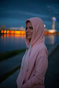 Side view portrait of woman wearing pink hood standing in city during dusk