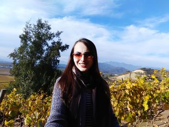 Portrait of smiling young woman standing by trees against sky