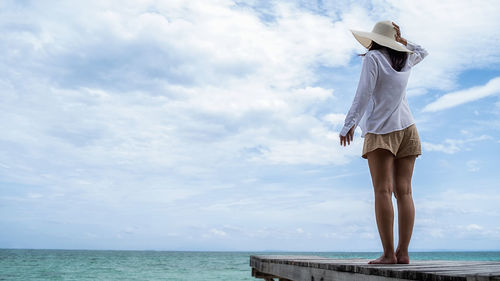 Rear view of woman standing by sea against sky