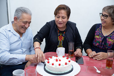 An older man with his friends celebrating a birthday, cutting a cake at an indoor party. old 