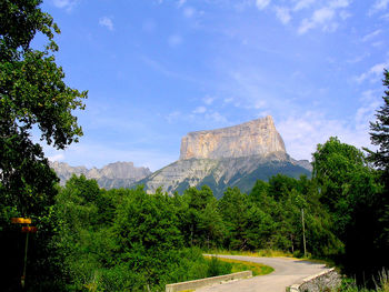 Road amidst trees with mont aiguille against sky