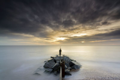 Rear view of man photographing while standing on rocks by sea during sunset