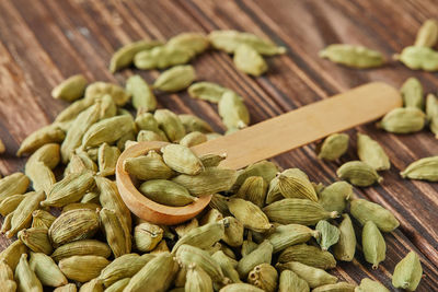 Green cardamom with wooden spoon scattered over vintage wooden background