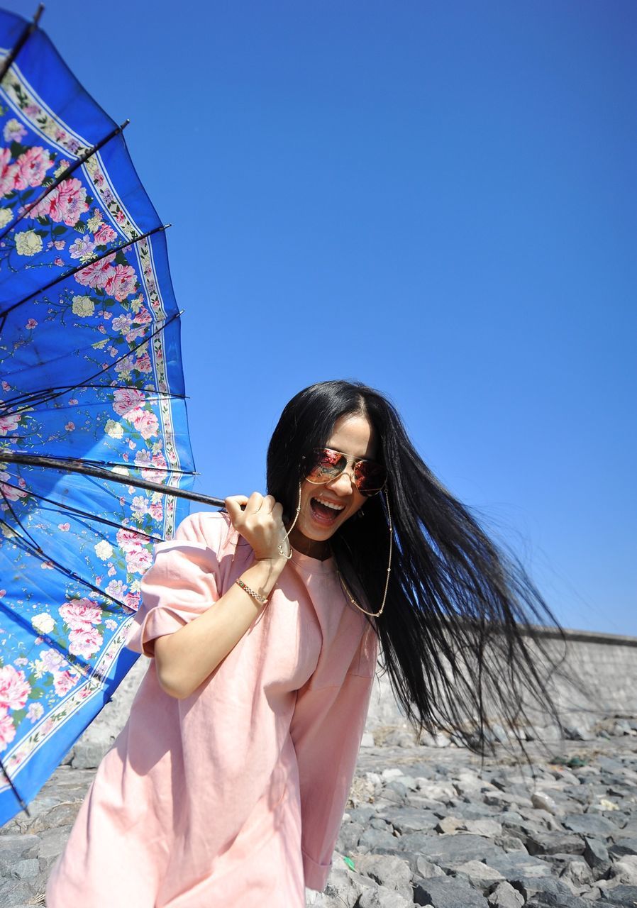 young adult, young women, lifestyles, person, leisure activity, portrait, looking at camera, smiling, front view, clear sky, long hair, sunglasses, casual clothing, happiness, standing, low angle view, waist up