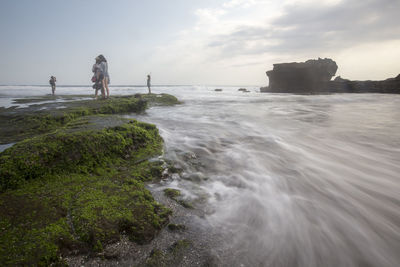 Friends standing on rock by sea against sky