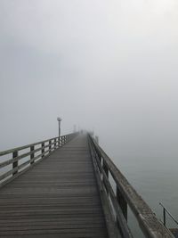 Wooden footbridge over pier against sky