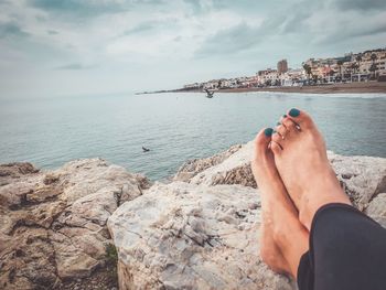 Low section of person on rock by sea against sky