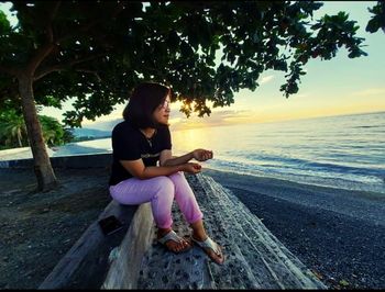 Woman sitting at beach against sky during sunset