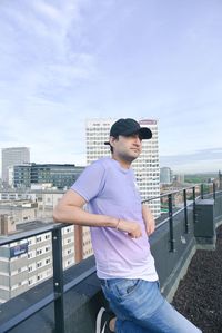 Young man standing against railing in city against sky