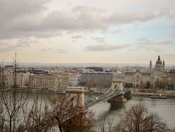 Bridge over river in city against cloudy sky