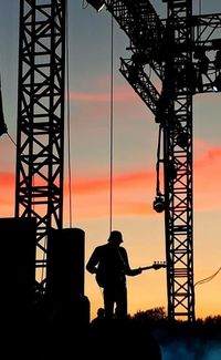 Silhouette man standing at amusement park against sky during sunset