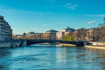 Bridge over river by buildings against blue sky