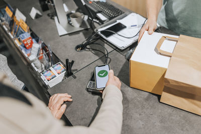 Cropped image of male customer scanning credit card reader through smart phone at checkout in electronics store