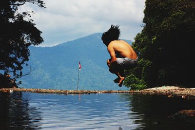 Shirtless man jumping in lake against sky