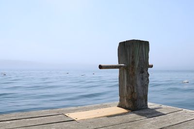 Wooden post on pier by sea against clear sky
