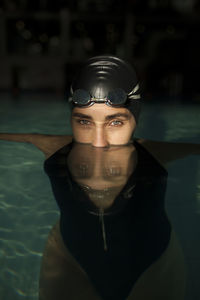 Young beautiful woman in the indoor pool, wearing black swimsuit, look at camera