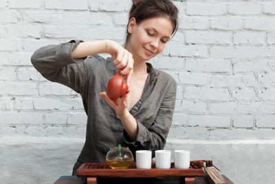 Woman pouring tea in mug against brick wall