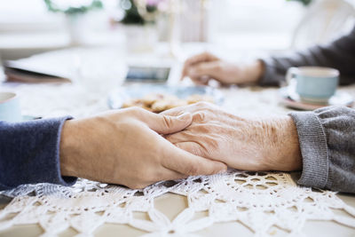 Cropped image of caretaker consoling senior man at dining table