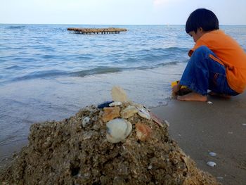 Boy on rock at beach against sky