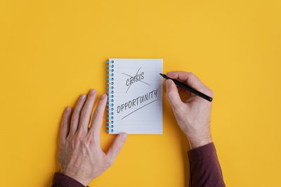 Midsection of woman reading book against yellow wall