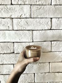 Cropped hand holding coffee against wall