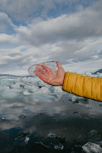 Male hand in yellow jacket holding black piece of ice in the glacier lagoon in iceland