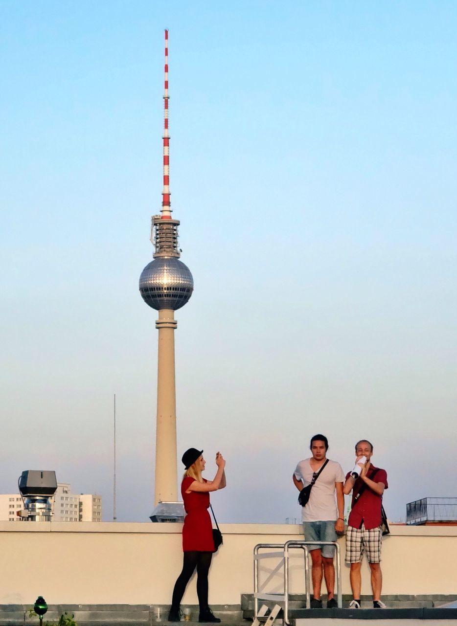 clear sky, lifestyles, leisure activity, architecture, built structure, casual clothing, copy space, tower, full length, building exterior, tourism, travel, men, travel destinations, standing, capital cities, communication, boys