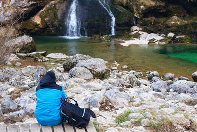 Rear view of woman sitting on rock by river