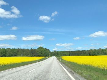 Yellow road amidst field against sky