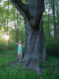 Woman standing by tree trunk in forest