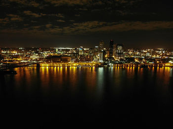 Illuminated buildings by river against sky at night