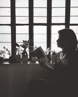 Side view of woman using mobile phone at window