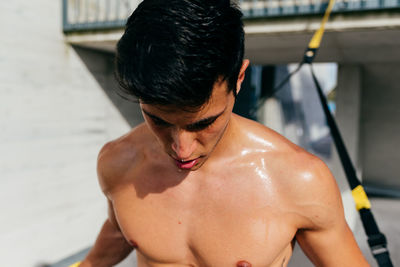 Determined male athlete with muscular body training on street with trx ropes and looking away