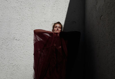 Portrait of young woman standing against wall