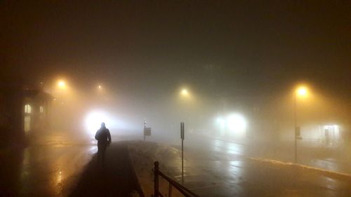 Silhouette woman standing on illuminated street light at night during winter