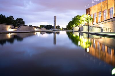 Illuminated buildings by river against sky in city